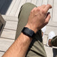 Ecoband 5.0 in Black worn on the wrist, seated on a sunlit wooden deck (black)
