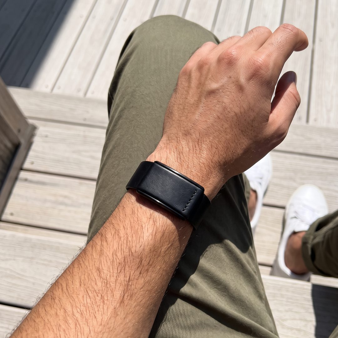 Ecoband 5.0 in Black worn on the wrist, seated on a sunlit wooden deck (black)