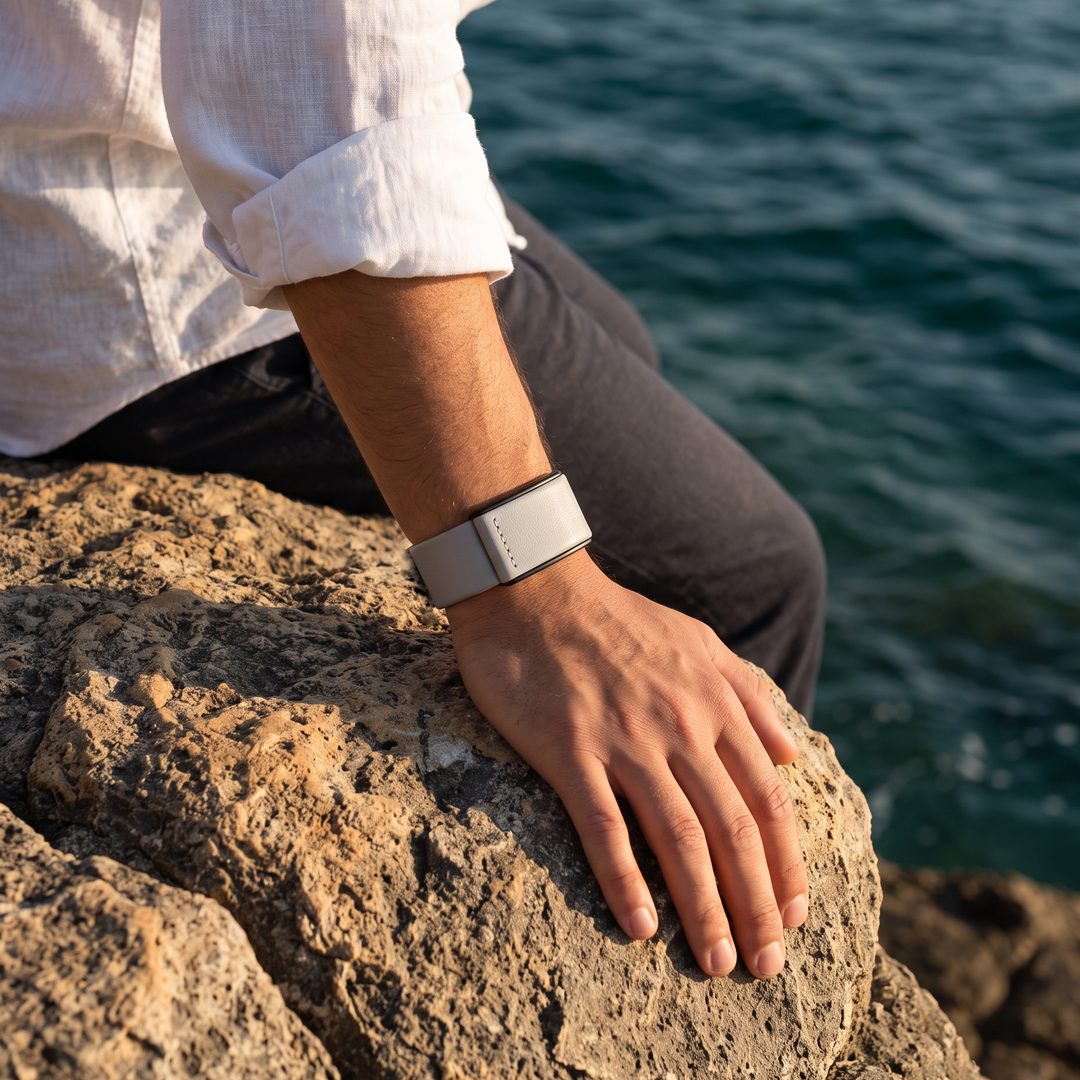 Ecoband 5.0 in Cloud worn on the wrist, hand resting on coastal rock by the sea (cloud)